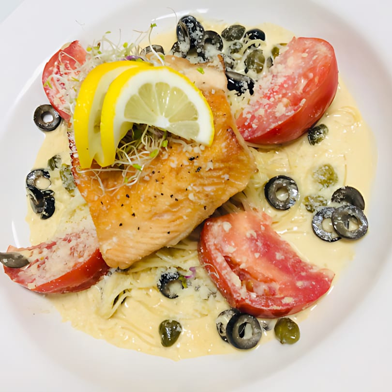 Ishy's Grill's salmon pasta with creamy sauce, tomatoes, olives, capers, and lemon slices.