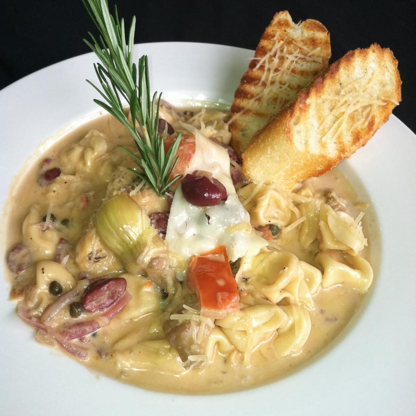 Creamy tortellini pasta dish with artichoke hearts, olives, and toasted bread at Ishy's Grill.
