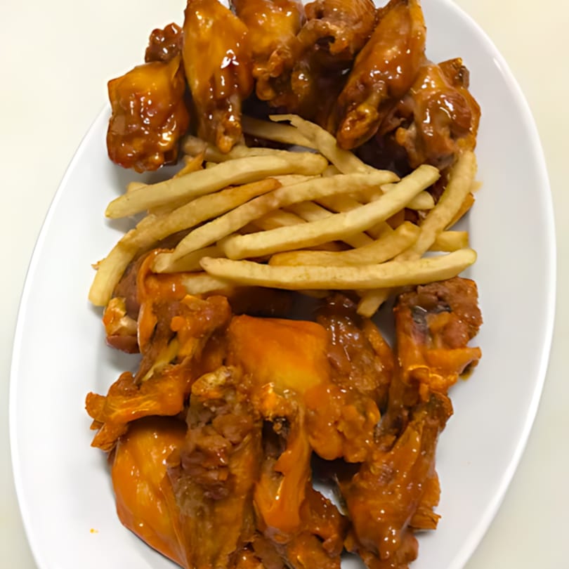 A white platter filled with golden-brown Ishy's Grill chicken wings and a pile of french fries.