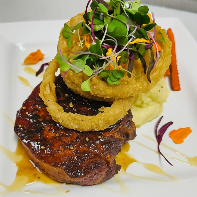 Ishy's Grill's American dish features a glazed steak, onion rings, mashed potatoes, and microgreens.