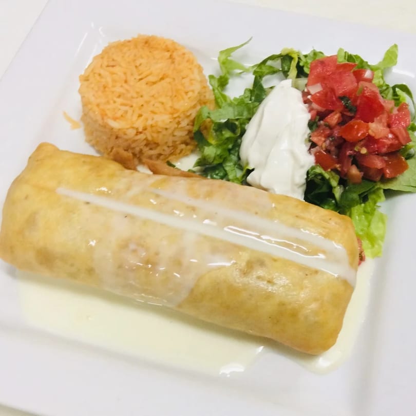 A golden-brown chimichanga drizzled with white sauce, served with rice, lettuce, sour cream, and pico de gallo.