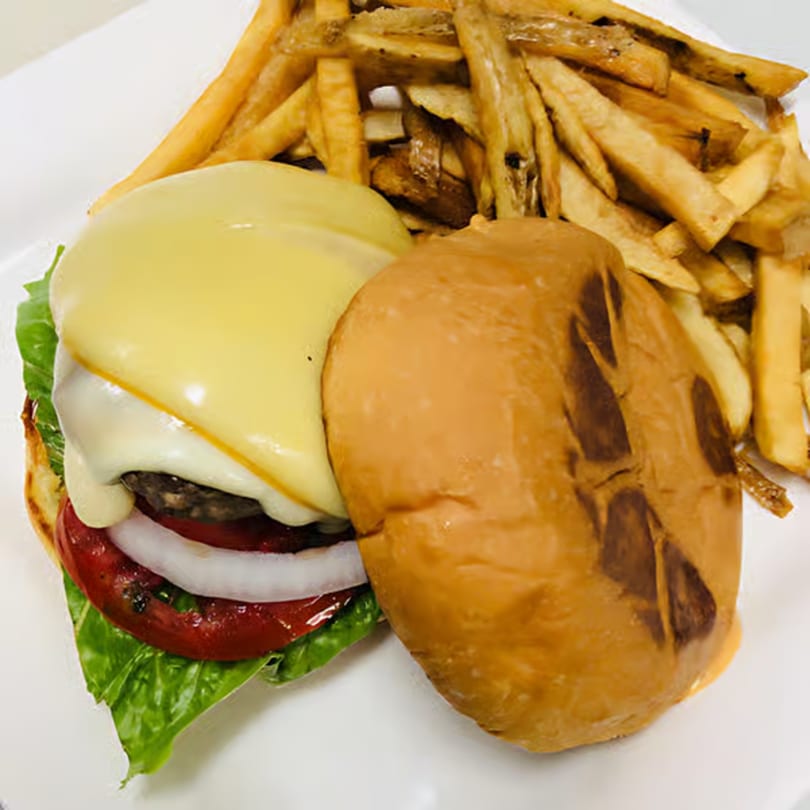 A cheeseburger with lettuce, tomato, and onion, served with a side of golden-brown french fries.